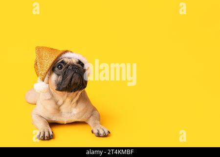 Niedlicher Mops mit Weihnachtsmann-Hut auf gelbem Hintergrund Stockfoto