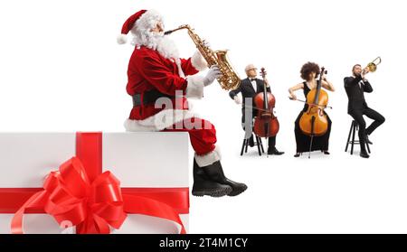 weihnachtsmann sitzt auf einem Geschenk und spielt Saxophon mit einer Musikband auf Cello und Posaune isoliert auf weißem Hintergrund Stockfoto