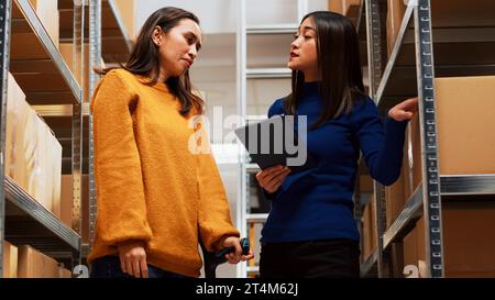 Eine junge Frau mit Krücken, die im Depot Teamarbeit macht und sich Kartons in Regalen und Regalen ansieht. Weibliche Eigentümerin und Angestellte, die mit Waren im Lagerraum arbeiten. Handgeführte Aufnahme. Stockfoto