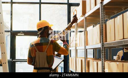 Zwei männliche Mitarbeiter, die im Depot mit Scanner und digitalem Tablet in der Logistik arbeiten, scannen Fracht mit Barcodes in Regalen. Leute, die Inventar mit Lagerboxen machen. Stativaufnahme. Stockfoto