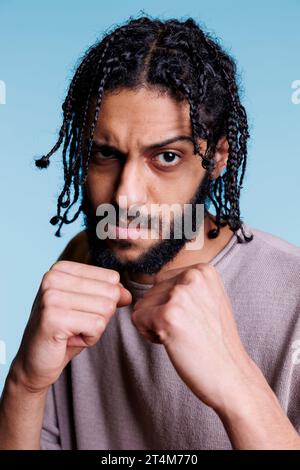 Ernsthafter arabischer Boxer mit geballten Fäusten in Kampfposition. Selbstbewusste Person, die Stärke zeigt, während sie in Boxstellung steht und bereit ist, das Porträt anzugreifen Stockfoto