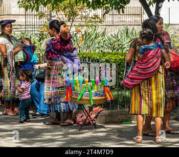 Guatemala, La Antigua - 20. Juli 2023: Einheimische Frauen und Kinder in farbenfroher traditioneller Kleidung hängen zusammen, während sie im grünen Park Spielzeug verkaufen Stockfoto