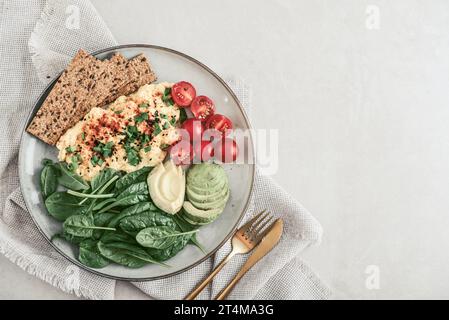 Rührei mit Kirschtomaten, frischen Spinatblättern, Avocado und Knäckebrot auf einem Teller, Blick von oben Stockfoto