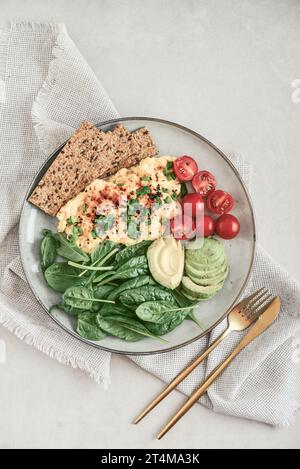 Rührei mit Kirschtomaten, frischen Spinatblättern, Avocado und Knäckebrot auf einem Teller, Blick von oben Stockfoto