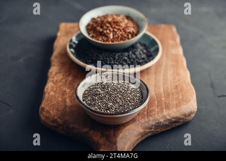 Schwarze Sesam-, Flachs- und Chiasamen in Keramikplatten auf dunklem Hintergrund Stockfoto