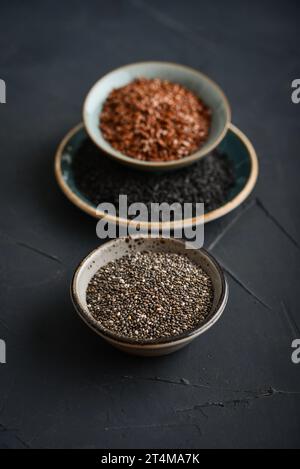 Schwarze Sesam-, Flachs- und Chiasamen in Keramikplatten auf dunklem Hintergrund Stockfoto