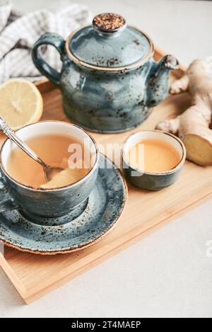 Ingwertee mit Zitrone in einer blauen Tasse mit Ingwerwurzel und Honig auf einem Bambustablett auf einem hellen Hintergrund Nahaufnahme Stockfoto