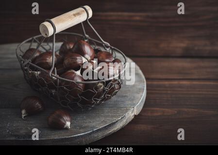 Essbare Kastanien in einem Metallkorb auf hölzernem Hintergrund, Draufsicht Stockfoto