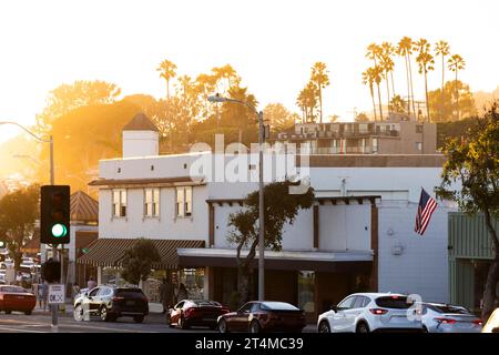 Laguna Beach, Kalifornien, USA - 3. August 2023: Das Licht des Sonnenuntergangs scheint durch Palmen und eingerahmt von historischen Gebäuden in der Innenstadt von Laguna Beach. Stockfoto