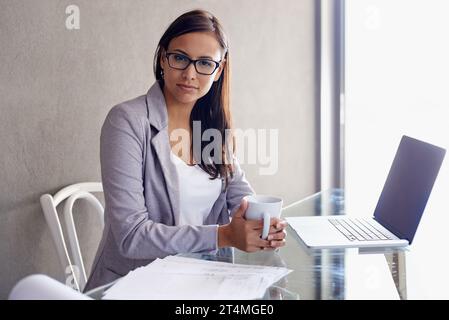 Eine Frau, die ihr Geschäft kennt. Eine attraktive junge Geschäftsfrau, die eine Kaffeepause an ihrem Schreibtisch macht. Stockfoto