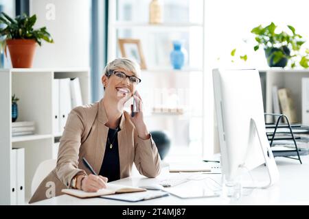 Sie ist immer bereit, für ihre Kunden extra zu arbeiten. Eine junge Geschäftsfrau, die Notizen schreibt, während sie im Büro auf einem Handy spricht. Stockfoto