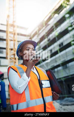 Ein Bauunternehmer mit intelligentem Bauwesen verwendet intelligente Tools. Eine junge Frau, die ein Smartphone benutzt, während sie auf einer Baustelle arbeitet. Stockfoto