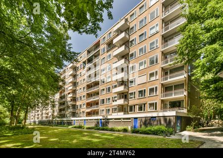 Ein Appartementgebäude mit vielen Fenstern und Ballen an der Seite, umgeben von üppigen grünen Bäumen im Sommer Stockfoto