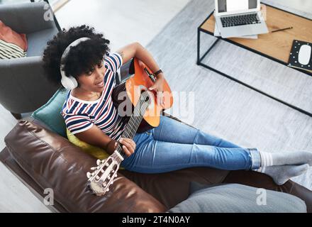 Gitarre zu spielen gibt mir ein gutes Gefühl. Eine Frau, die Kopfhörer trägt, während sie zu Hause Gitarre spielt. Stockfoto