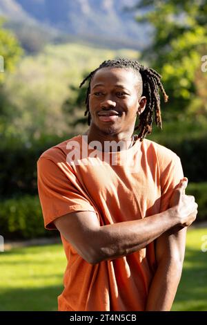 Glücklicher afroamerikaner mit Dreadlocks, die im sonnigen Garten lächeln Stockfoto