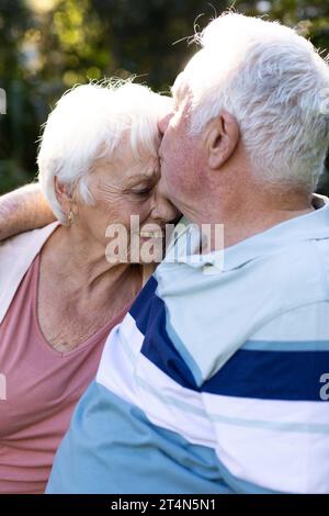 Glückliches kaukasisches Seniorenpaar, das sich im sonnigen Garten umschließt und küsst, Kopierraum Stockfoto