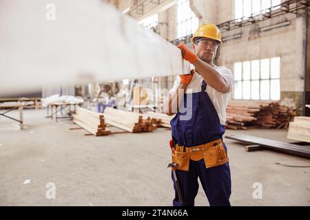 Serious Mann Baumeister trägt Holzbrett auf der Baustelle Stockfoto