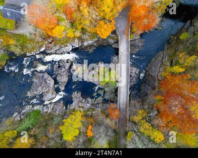 Blick aus der Vogelperspektive auf die alte Brücke über den Fluss Moriston, umgeben von Wäldern in Herbstfarben in Invermoriston, Schottland, Großbritannien Stockfoto