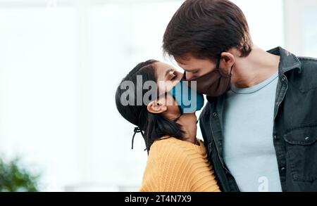 Wenn du 2020 flirtest, wirst du mit mir in Quarantäne gehen. Ein junges Paar küsst sich, während es zu Hause Masken trägt. Stockfoto