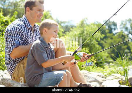 Angeln in der Sonne mit Dad. Seitenansicht eines Vaters, der mit seinem Sohn sitzt und fischt. Stockfoto