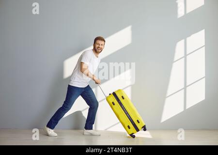 Junger glücklicher bärtiger Mann mit Koffer geht in Sommerferien isoliert auf grauem Hintergrund. Stockfoto