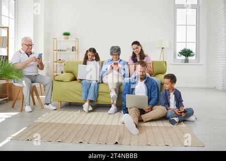 Große Familie, die verschiedene elektronische Geräte verwendet, während sie zu Hause auf dem Sofa sitzt Stockfoto