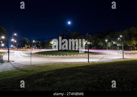 Ein Kreisverkehr in einer schnellen Straße in einer italienischen Stadt bei Nacht, mit einigen Autolichtern in beide Richtungen. Stockfoto