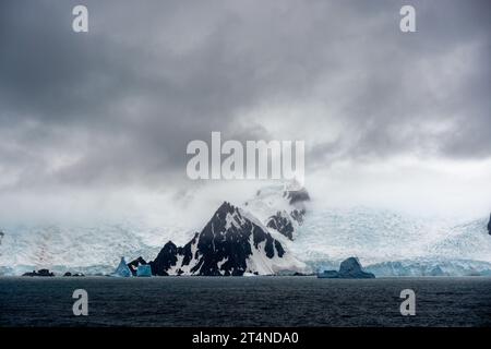 Niedrige Wolke über Eis und schneebedeckte Berge mit Eisbergen im Vordergrund. antarktische Halbinsel. antarktis Stockfoto