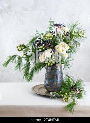 Wunderschöner Winterstrauß in Vase. Blumenarrangements mit Rosen, Tannenzweigen, Winterbeeren, Eukalyptus und eryngium. Weihnachtsblumendekoration. Stockfoto