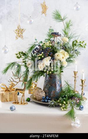 Weihnachtsdekoration, Kerzen, Geschenkboxen und Blumenstrauß. Winterarrangements mit Rosen, Tannenzweigen, Winterbeeren. Weihnachtsstillleben. Stockfoto