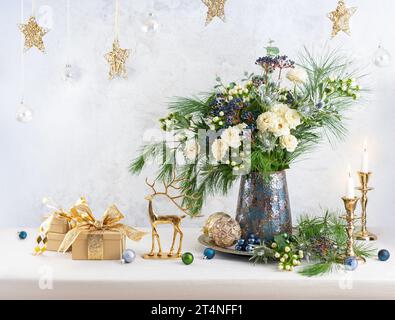 Weihnachtsdekoration, Kerzen, Geschenkboxen und Blumenstrauß. Winterarrangements mit Rosen, Tannenzweigen, Winterbeeren. Weihnachtsstillleben. Stockfoto