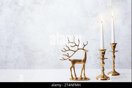 Gemütliches Stillleben mit brennenden Kerzen und Hirschfigur auf pastellfarbenem Hintergrund. Weihnachtskomposition Dekoration des Heims. Stockfoto