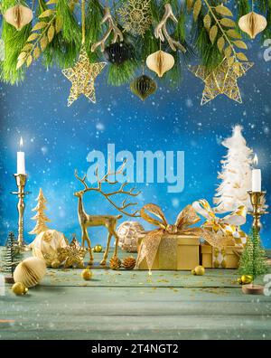 Festliche Komposition zu Weihnachten oder Neujahr. Tannenzweige, Kerzen, goldene Weihnachtsdekorationen, Kugeln, Hirsche und Geschenkboxen auf Holztisch. Stockfoto