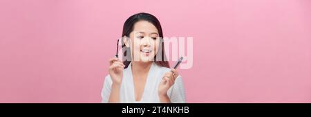Schöne junge Frau mit Make-up-Pinsel, die schwarze Mascara auf Wimpern auf rosa Hintergrund aufträgt Stockfoto