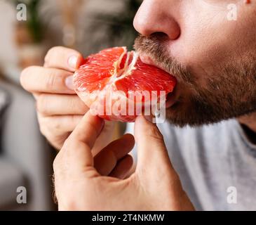 Der Mann isst rote Grapefruit aus nächster Nähe. Gesunde Ernährung. Stockfoto