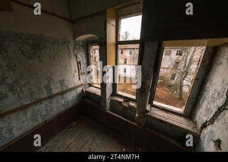 Von oben blickte man auf das Innere des Zimmers mit Holzfußboden, schäbige, unbeschädigte, abgenutzte Wände, die Farbe abblätterten, und die Fenster blickten auf das verlassene Gebäude mit Bäumen im Tageslicht Stockfoto