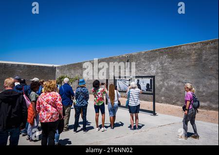 29.10.2023, xovx, Politik, Reise. Robben Island - Gefängnisinsel vor Kapstadt Besuchergruppe und Schaubild Nelson Mandelas im Gefängnishof des Zellenblocks des Hochsicherheitstrakts auf der Gefängnisinsel Robben Island vor der Küste von Kapstadt, in dem Nelson Mandela über 18 Jahre seiner Gefangenschaft in Einzelhaft inhaftiert wurde. Der spätere Präsident Südafrikas Nelson Mandela verbrachte hier von 1964 bis 1982 seiner insgesamt 27-jährigen Gefangenschaft, zumeist bei Einzelhaft und unmenschlichen Bedingungen. Robben Island ist eine Insel zwölf Kilometer vor der südafrikanischen Stadt Kapst Stockfoto