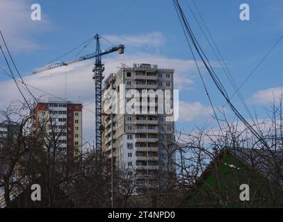 Ein Blick auf ein Gebäude, das sich im Bau befindet, mit einem Kran in der Nähe vor blauem Himmel. Einige halten Seile im Vordergrund. Stockfoto