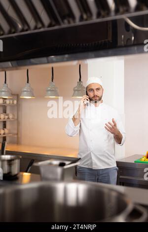 Konzentrierter kaukasischer Koch, der über Smartphone spricht, gestikuliert in der Küche des Restaurants, Kopierraum Stockfoto