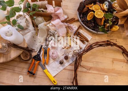 Meisterkurs, Anleitung, DIY, wie man Weihnachtskranz für den Advent macht. Auf Holztisch: Tannenzweige, Eukalyptus, Kranzbasis, Bänder, Schere, Dr Stockfoto