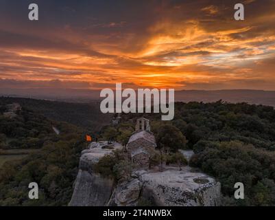 Luftaufnahme der Klippen und der Eremitage von Sant Feliuet de Savassona bei einem roten Sonnenuntergang (Osona, Barcelona, Katalonien, Spanien) Stockfoto