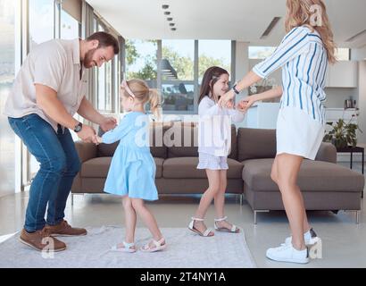 Kaukasische vierköpfige Familie, die im Wohnzimmer zu Hause Spaß macht und zusammen tanzt. Glückliche kleine, verspielte Mädchen, die sich mit Mom und Dad verbinden. Sorgenfrei Stockfoto