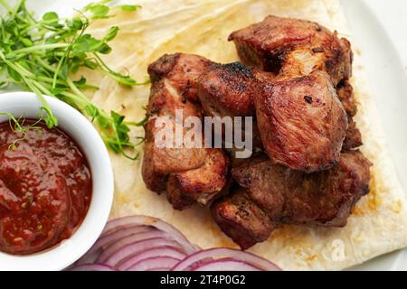 Gebratener Shish Kebab mit Lavasch, Sauce, Microgreen und Zwiebel, auf einem weißen Teller, auf grauem Grund Stockfoto