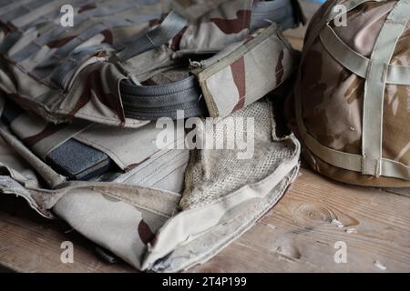 Ein Militärhelm eines ukrainischen Soldaten mit einer schweren kugelsicheren Weste auf einem Holztisch im Innenraum des Kontrollpunktes Stockfoto