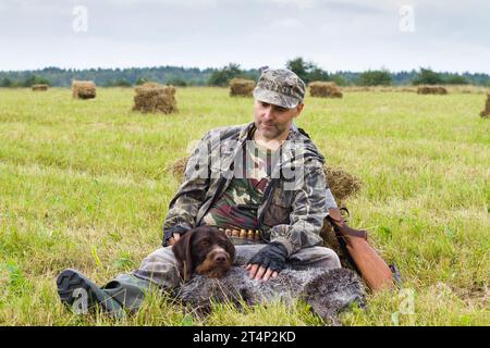 Jagdhund ruht während der Herbstjagd zu Füßen des Jägers auf dem Heufeld Stockfoto