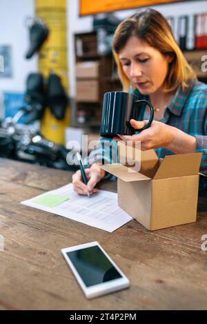 Frau, die neue Waren für den Verkauf in einem lokalen Geschäft vorbereitet. Paketzustellung und E-Commerce-Konzept. Stockfoto