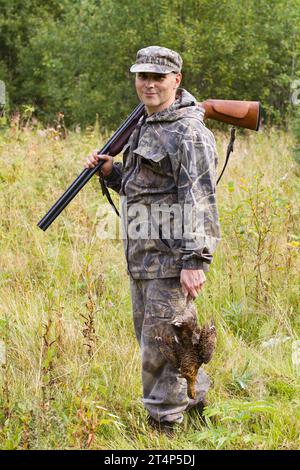 Der Jäger sieht sich mit der Schrotflinte auf der Schulter und dem abgestürzten Spiel in der Hand um Stockfoto