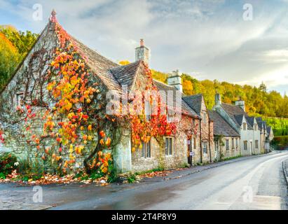 Eine wunderschöne Herbstszene eines alten Cotswolds Cottage in Castle Combe, bedeckt mit Efeu und leuchtend roten und orangen Blättern. Stockfoto