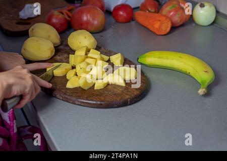 Schneiden Sie Kartoffeln mit einem Messer auf einem Schneidebrett in kleine Stücke. Abwicklung Stockfoto