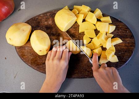 Schneiden Sie Kartoffeln mit einem Messer auf einem Schneidebrett in kleine Stücke. Abwicklung Stockfoto